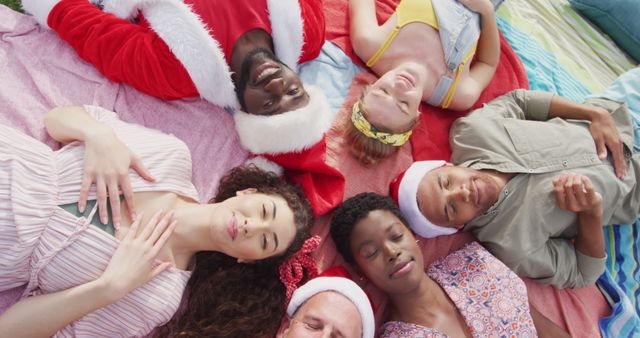 Six diverse happy friends celebrating christmas in costumes, lying outdoors waving to camera. Christmas, celebration, tradition, friendship, inclusivity and lifestyle concept.