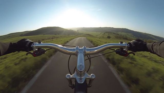 Pov cycling down sunlit country road from handlebars, adventure cycling lifestyle