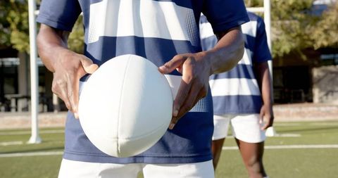 Rugby Player Holding Ball in Navy Striped Jersey Preparing for Kick on Sunny Pitch