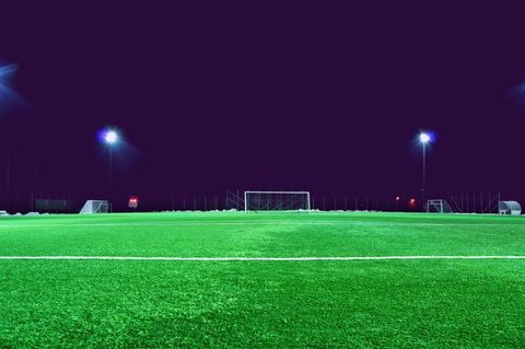 Nighttime soccer field glowing under stadium floodlights featuring empty goal and vibrant turf