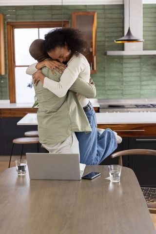 Joyful couple embracing and lifting partner in modern kitchen with laptop on table