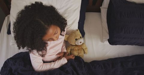 Young Girl Holding Teddy Bear Sitting on Bed