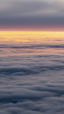 Vertical aerial video capturing sunrise glow above rolling cloud layer and pastel sky