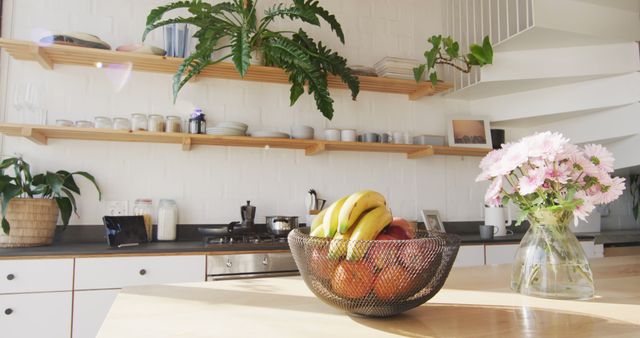 This vibrant modern kitchen features a chic combination of fresh fruit and floral decor. Sunlight streams through, illuminating wooden shelves stocked with dishes and plants. Ideal for promoting interior design services, home decor brands, or lifestyle blogs focused on minimalist and contemporary living spaces.