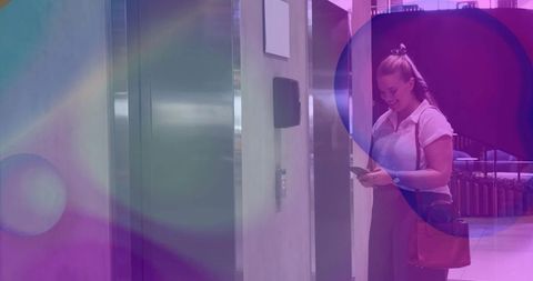 Businesswoman checking smartphone beside elevator in office lobby