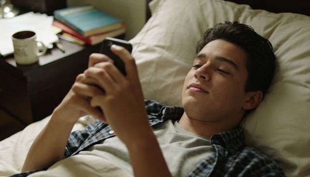 Teen relaxing in bed while using smartphone for messaging and entertainment