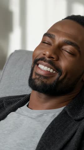 Vertical video of Black man reclining in lounge chair, smiling and enjoying calm relaxation