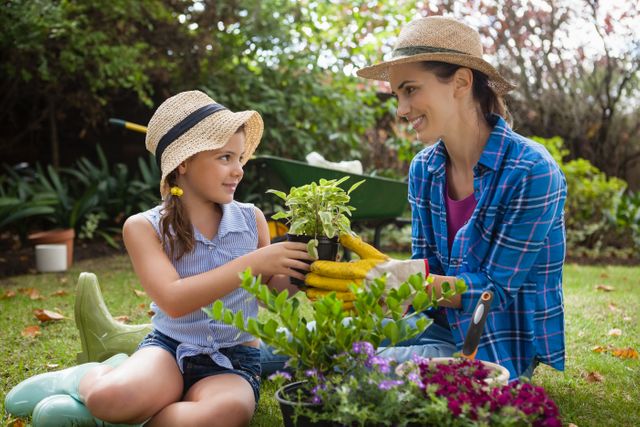 Smiling daughter and mother with potted plants sitting on grass in backyard