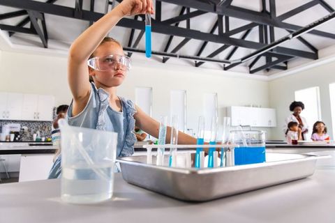 Young girl conducting stem experiment with blue test tubes in modern classroom lab