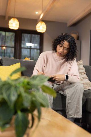 Non-binary person writing on tablet in cozy living room with soft pendant lighting