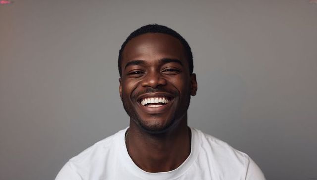 Confident young man laughing in white t-shirt with bright smile studio headshot