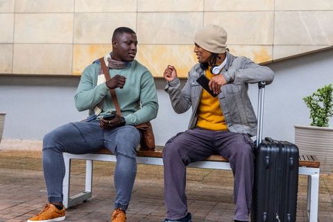 Friends chatting on transit bench with suitcase and smartphones, urban travel lifestyle