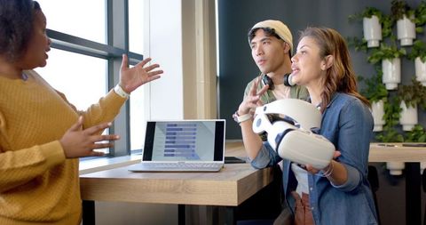 Multiracial team collaborating on vr prototype with laptop ui in modern workspace