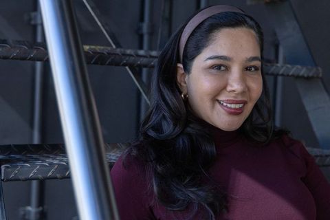 Confident young woman smiling on industrial metal stairs wearing burgundy turtleneck