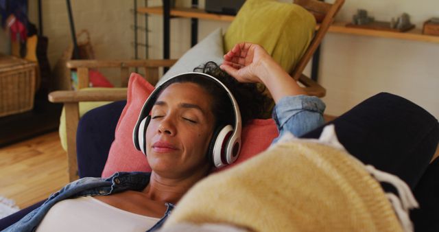 Image depicting a woman lying on a couch at home, wearing headphones and enjoying music. Suitable for use in lifestyle, relaxation, home comfort, and leisure activity content. Ideal for wellness, music enjoyment, and at-home relaxation themes.