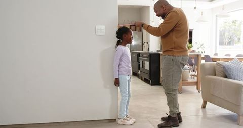 Father and daughter tracking height at home in modern kitchen