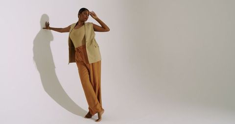 Woman in stylish beige vest and brown trousers against white wall
