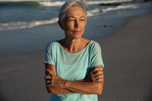 Senior woman stands on the beach with the ocean in the background, enjoying a sunny day. Ideal for promoting senior travel, beach vacations, healthy living, and outdoor activities for the elderly.