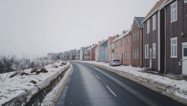 Winding wet asphalt road lining colorful wooden houses in snowy village fog scene