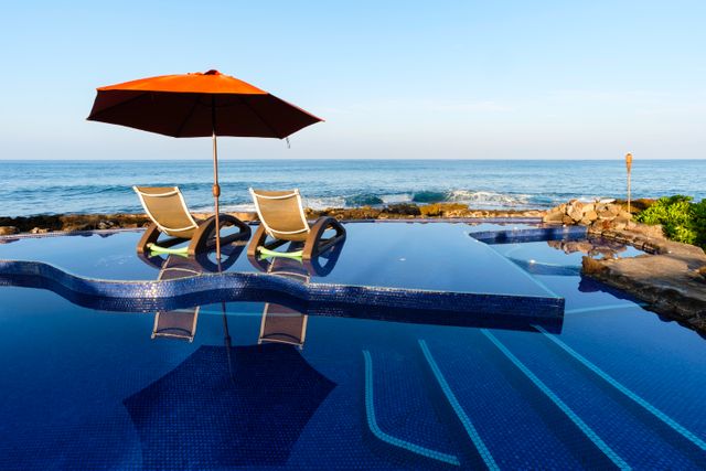 Infinity pool with two sun loungers and umbrella, overlooking ocean during golden hour. Ideal for travel brochures, luxury vacation magazines, and relaxation-themed websites.