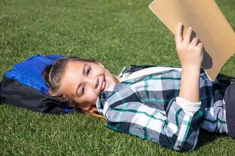 Smiling girl relaxing outdoors with book on warm sunny day