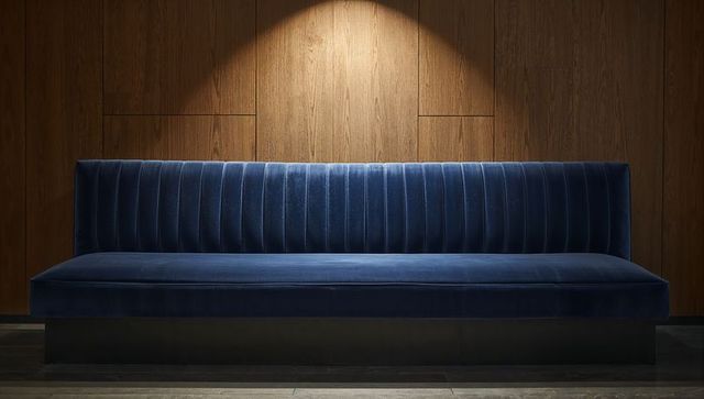 Deep blue velvet channel-tufted bench under spotlight against warm wood panel backdrop