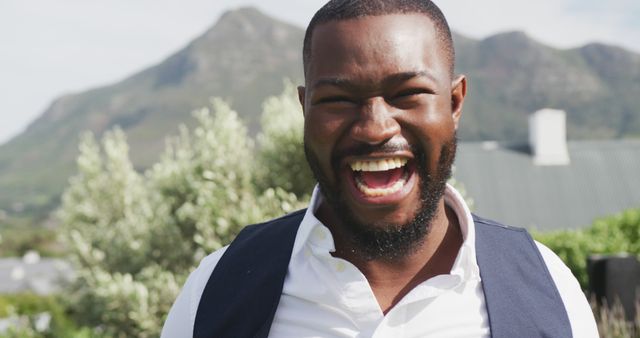 Image portrait of happy african american groom laughing to camera at outdoor wedding. Marriage, love, happiness and inclusivity concept.