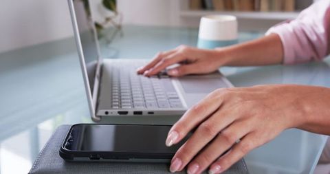Mid-adult woman multitasking with laptop and smartphone in home office