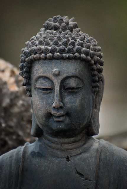 Close-up of a weathered Buddha statue's tranquil face in an outdoor setting. Ideal for use in articles about spirituality, meditation practices, Buddhist culture, Zen environments, and mindfulness. Suitable for websites, blogs, educational materials, and decorative purposes.