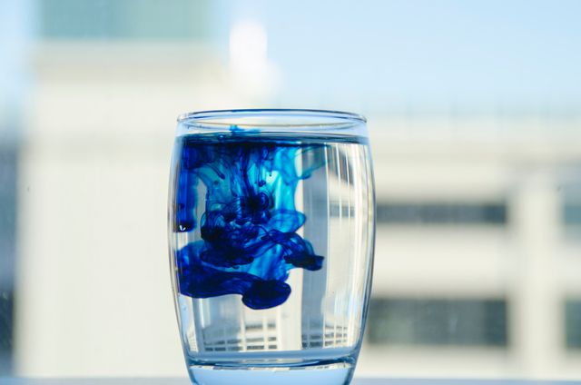 Blue ink dispersing in clear water inside a glass cup, creating mesmerizing patterns. This can be used for educational purposes in science experiments related to diffusion, chemistry, or fluid dynamics. It also presents an abstract artistic background fit for various creative projects.
