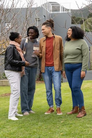Multiracial friends laughing and chatting on autumn lawn near modern gray building