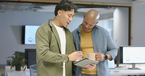 Collaborating over tablet and coffee by diverse male coworkers in modern open-plan office