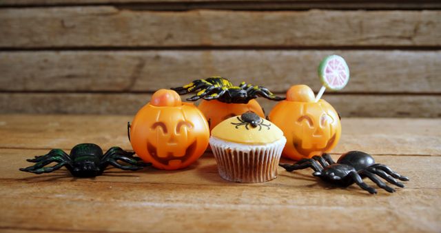 Halloween-themed decorations include pumpkin containers, a cupcake with an icing design, and plastic spiders on a wooden backdrop, with copy space. These festive items evoke the spirit of Halloween, perfect for seasonal celebration and decoration.