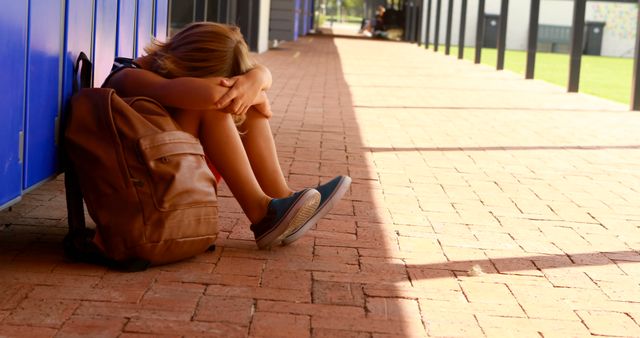 Teen student sitting on school corridor with head down, feeling stressed and upset. Backpack beside the student. Useful for illustrating mental health, academic issues, and teenage struggles.