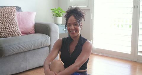 African american woman smiling sitting on floor after home workout in bright living room