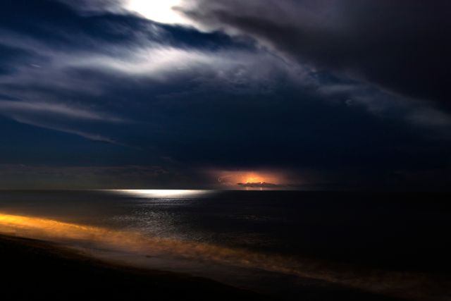Capture mood with dramatic coastal night scene featuring lightning illuminating dark cloud over calm ocean. Useful for nature, travel, and climate change themes. Perfect for highlighting power, beauty darkness of nature.