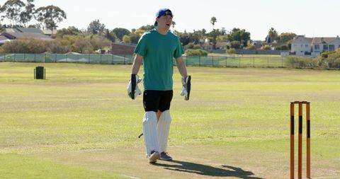 Teen wicketkeeper celebrating dismissal on sunny club cricket pitch with gloves and pads