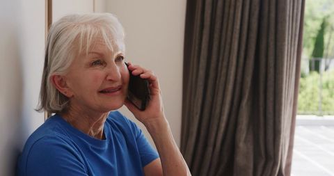 Senior Woman Relaxing by Window with Smartphone