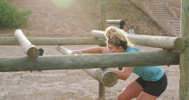 A female trail runner climbing through a wooden obstacle course outdoors. She is wearing a blue shirt and black shorts and focusing on completing the challenge. Ideal for promoting outdoor fitness activities, showing determination and strength, or use in articles about obstacle races and athletic training.