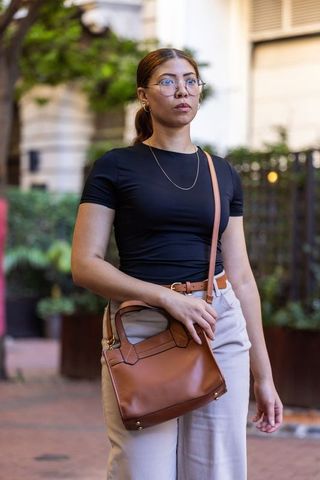 Urban professional woman walking carrying tan leather handbag wearing round glasses
