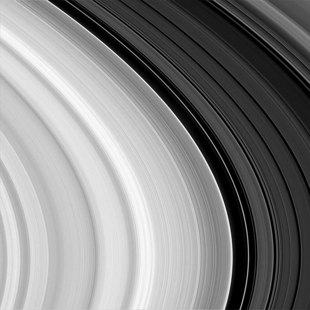 This image NASA Cassini spacecraft shows subtle, wavelike patterns, hundreds of narrow features resembling a record grooves in Saturn outer B-ring, and a noticeable abrupt change in overall brightness beyond the dark gap near the right. 