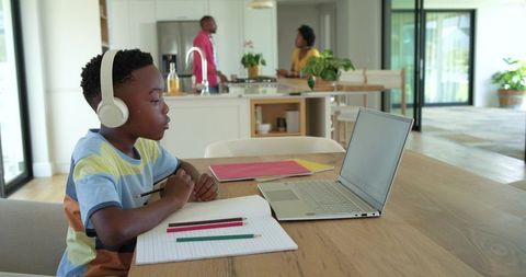 African american family home boy wearing headset doing remote learning at kitchen table