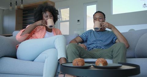 Joyful couple relaxing with hot drinks at home