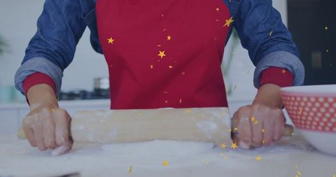 Home baking woman rolling dough with wooden pin wearing red apron and denim shirt