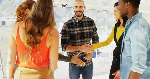 Shaking hands and greeting among diverse young professionals in bright modern glass office