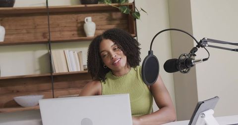 African american woman recording podcast in home studio with laptop, microphone and tablet