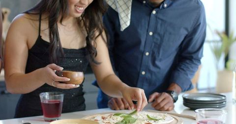 African american couple preparing homemade pizza on kitchen island with fresh basil