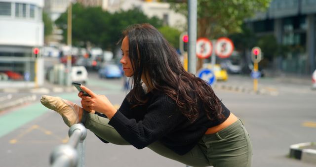 Beautiful woman using mobile phone while leg stretched on a railings in the city. City in the background 4k