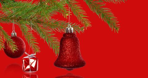 Christmas Decorations Hanging from Pine Branches over Red Background