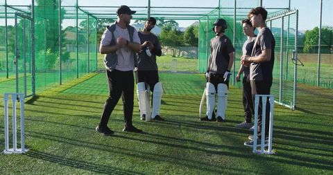 Coach gesturing while training four cricket players in outdoor net practice with pads